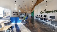 Located at 302 Morgantown Rd in Bowling Green, Kentucky, this single-floor collaborative workspace is thoughtfully designed to inspire creativity and productivity. The interior is anchored by striking polished concrete floors that flow seamlessly throughout, reflecting abundant natural light that pours in through generous windows positioned along the soaring walls.

The main open area features dramatic high ceilings with exposed pendant Edison bulb lighting suspended at varying heights, lending an industrial-modern aesthetic. A bold "Kentucky Owns My Mind" wall mural and Kentucky-themed décor establish a strong sense of local identity. This central zone accommodates a dedicated computer workstation row, a communal high-top table with bar stools, and a relaxed lounge seating arrangement complete with a large sectional sofa and area rug.

A wood-accented dividing wall adds warmth and architectural interest, while a glass-walled room offers a transparent, light-filled private workspace. A cozy lounge nook features upholstered armchairs, a vintage upright piano, wall-mounted shelving, and a large window framing outdoor views — ideal for informal meetings or quiet focus.

An intimate breakout corner, painted in a vibrant blue, displays a creative inspiration collage wall and is furnished with comfortable blue accent chairs. The space balances energetic communal zones with quieter areas, making it a versatile environment suited for individuals and collaborative teams alike.