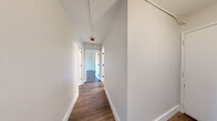 Located at 68 Pearl St in Brookline, MA, this two-bedroom, two-bathroom residence offers a thoughtfully updated single-level layout designed for comfortable everyday living. Consistent hardwood-style flooring flows throughout the unit, tying together each room with a warm, cohesive aesthetic.

The kitchen stands out with white shaker cabinetry, white quartz countertops, a hexagonal tile backsplash, matte black hardware, and a full suite of stainless steel appliances including a refrigerator, range, dishwasher, and microwave. A window above the sink brings in natural light and an outdoor view of the surrounding neighborhood.

The combined kitchen and living area provides a practical open layout, while a long, clean hallway with crisp white walls and dark hardware connects the private areas of the home. Both bedrooms are well-proportioned and feature large windows that frame tree-lined views, neutral walls, and the same rich flooring found throughout.

The two bathrooms offer distinct configurations: one includes a full soaking tub and shower combination with marble-style surround and matte black fixtures, while the second features a sleek walk-in shower with white surrounds and a white vanity. A dedicated closet adds valuable storage. The overall design is clean, modern, and move-in ready.