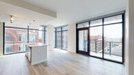 Located at 401 Race St in the heart of Cincinnati's downtown, this contemporary single-floor unit showcases a thoughtfully designed open layout filled with natural light. The living and dining area is anchored by expansive floor-to-ceiling windows framed in sleek black metal, offering sweeping views of the surrounding urban streetscape, including notable historic architecture. Light-toned hardwood flooring runs throughout the main living spaces, reinforcing a clean, modern aesthetic.

The kitchen is a standout feature, centered around a generous island with a white quartz countertop and an undermount sink. Rich walnut-toned cabinetry lines the walls, complemented by stainless steel appliances, a built-in microwave, and pendant lighting above the island. Track lighting provides additional illumination across the cooking area.

The bedrooms feature plush carpeting and neutral wall tones, creating a calm retreat from the open living spaces. Multiple rooms offer direct access to outdoor balconies through black-framed glass doors, extending the city views into private outdoor areas.

The bathrooms are finished with floating wood-toned vanities, white quartz countertops, large mirrors, and walk-in shower enclosures, presenting a polished, contemporary look throughout. The overall ambiance is bright, urban, and refined.
