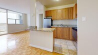 This efficiently designed 1-bedroom, 1-bathroom unit offers a thoughtful layout across a single floor. Warm parquet wood flooring flows throughout the living areas and bedroom, lending a timeless character to the space. The open-concept kitchen and living room area serves as the heart of the unit. The kitchen is equipped with warm-toned wood cabinetry, granite countertops, stainless steel appliances including a refrigerator and range, and a peninsula that provides additional workspace and separates the kitchen from the living area. The spacious living room is bathed in natural light through a large floor-to-ceiling window and sliding glass door that opens directly onto a private balcony. From the balcony, sweeping views of the surrounding residential neighbourhood and a distant city skyline can be enjoyed. The bedroom is a comfortable, well-proportioned room featuring the same parquet flooring and a built-in sliding door closet for ample storage. A hallway with tile flooring connects the main areas to the bathroom, which includes a full soaking bathtub with tiled surround, toilet, and vanity with mirror. Light marble-style tile flooring is found in the hallway and bathroom, providing a clean transition between spaces.