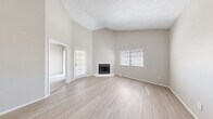 This well-appointed 2-bedroom, 1-bathroom single-floor home offers a thoughtfully designed layout across a comfortable footprint. The living room immediately impresses with its soaring vaulted ceilings and textured finish, anchored by a corner fireplace and flanked by multiple windows that invite abundant natural light. Light-toned wood-style flooring runs throughout the main living areas, contributing to a clean, cohesive aesthetic. The kitchen is efficiently laid out in a galley style, featuring white cabinetry, light countertops with a double-basin sink, a dishwasher, and black appliances including a refrigerator and electric range. A pass-through ledge connects the kitchen to the adjacent living area, enhancing the open feel. Both bedrooms are carpeted and offer a quiet, neutral atmosphere; the primary bedroom includes a ceiling fan and a window with natural light, while the second bedroom also features carpeting and closet access. The full bathroom is well-equipped with a wide vanity, light countertops, and ample mirror space. A dedicated in-unit laundry room accommodates a full-size washer and dryer with built-in shelving above. A hallway and closet complete the functional layout, making this home a practical and comfortable living space.