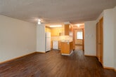 This single-floor unit offers a practical and functional layout designed for comfortable everyday living. The open-concept living and kitchen area is anchored by rich, dark hardwood-style flooring that extends throughout the main living spaces, complemented by a textured ceiling and a ceiling fan. The living area is bright and spacious, featuring a sliding glass door that opens to an outdoor space, allowing natural light to pour in and providing easy access to the exterior.

The kitchen is efficiently designed with light wood cabinetry, ample upper and lower cabinet storage, a central island unit housing the electric range, a dishwasher, a refrigerator, and a double sink. Under-cabinet fluorescent lighting enhances visibility, and the layout promotes a smooth workflow between cooking and dining areas.

The bedroom is generously sized, featuring plush carpeting, a large sliding-door closet for substantial storage, and a window with blinds that invites natural light while maintaining privacy. A baseboard heating unit ensures year-round comfort in both the bedroom and living areas.

The bathroom is clean and well-lit, featuring a full tub-shower combination, a single vanity with wood cabinetry, light countertops, a large mirror, and a Hollywood-style vanity light bar. Throughout the unit, warm wood-toned trim and neutral wall tones create a cohesive and welcoming atmosphere.