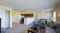 This single-floor residence offers a thoughtfully designed open-concept layout that connects the living, dining, and kitchen areas into one cohesive, comfortable space. The living area features plush carpeting and is anchored by a cozy seating arrangement, complemented by a ceiling fan that enhances air circulation and comfort. A sleek, dark coffee table adds a modern touch to the space.

The kitchen is well-appointed with stainless steel appliances, including a refrigerator and range, set against rich, dark wood cabinetry that provides ample storage. A peninsula-style breakfast bar serves as both a functional workspace and a natural divider between the kitchen and living areas, making it ideal for casual dining or entertaining.

Adjacent to the living space, a dining area accommodates a table and chairs, providing a dedicated spot for meals. Track lighting in the kitchen and ceiling fans throughout ensure the space is well-lit and comfortable year-round.

The neutral color palette, featuring light walls and warm-toned carpet, creates a bright and welcoming ambiance throughout. The open flow of the layout makes the space feel expansive and practical for everyday living.