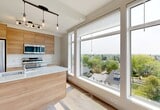 Located on University Avenue NW in Edmonton, Alberta, this thoughtfully designed one-bedroom, one-bathroom unit offers a clean, modern aesthetic throughout its efficiently utilized single floor. Light-toned luxury vinyl plank flooring runs seamlessly across the entire space, complementing the bright, neutral palette that defines each room.

The kitchen serves as the heart of the unit, anchored by a sleek island with a white quartz countertop and an undermount sink. Warm wood-toned cabinetry extends to the upper level, paired with stainless steel appliances including a refrigerator, built-in microwave, and range. A striking multi-bulb pendant light fixture hangs overhead, while large floor-to-ceiling windows flood the space with natural light and frame expansive treetop and cityscape views.

A hallway connects the main living area to the private quarters, featuring a distinctive full-height sliding barn door with bronze hardware — a stylish design detail that adds character to the otherwise minimalist interior. The bedroom offers a comfortable layout with a window for natural light and direct access to a well-organized built-in closet complete with shelving and a hanging rail.

The bathroom is finished with a wood-tone floating vanity, a backlit mirror, and a full tub-shower combination, maintaining the same clean, contemporary feel found throughout the unit.