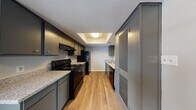 This single-floor residence offers a cohesive and functional layout designed for comfortable everyday living. The galley-style kitchen is a standout feature, showcasing dark grey cabinetry paired with granite-look countertops and a full suite of black appliances, including an electric range, refrigerator, and dishwasher. A distinctive tray ceiling with a central flush-mount light adds architectural interest overhead, while warm wood-look flooring runs the length of the kitchen. A louvered utility closet provides convenient additional storage within the kitchen area.

The living areas and bedrooms continue the warm wood-look flooring, creating a unified aesthetic throughout. The bedrooms are generously proportioned, each featuring neutral-toned walls and natural light streaming in through sizable windows fitted with blinds. Ceiling fans in select rooms enhance comfort. The bathroom is clean and straightforward, equipped with a full-size soaking tub and shower combination featuring a built-in niche surround, a toilet, and durable wood-look flooring. Neutral wall tones and white trim work are consistent across all rooms, giving the space a clean, move-in ready appearance throughout.