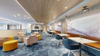 Located at 321 Main St in Hackensack, NJ, this thoughtfully designed commercial space offers a sophisticated and modern environment ideal for professional use. The single-floor layout spans a generously sized footprint, combining open collaborative zones with dedicated private workspaces. Distinctive blue patterned carpeting flows throughout the main areas, contrasting elegantly with warm wood-paneled ceilings and crisp white walls accented by recessed and linear LED lighting.

The open lounge and collaboration area features modular seating arrangements with blush and neutral-toned armchairs, vibrant yellow ottomans, and café-style tables with contemporary chairs — creating a dynamic environment suited for both casual meetings and focused work. A glass-enclosed conference or office area provides privacy while maintaining visual connectivity to the open floor, with floor-to-ceiling windows offering clear views of the surrounding Hackensack streetscape.

A glass-railed mezzanine-style overlook connects upper and lower levels, allowing natural light to permeate the space. A striking multi-pendant chandelier serves as a central architectural focal point. Built-in shelving and warm wood accents add texture and warmth, while large exterior-facing windows ensure abundant natural light throughout. The overall ambiance is polished, professional, and inviting.