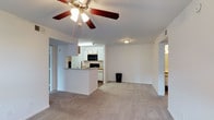 This single-floor, 2-bedroom, 2-bathroom residence offers a practical and comfortable layout designed for everyday living. The open-concept living and kitchen area serves as the heart of the home, creating a connected and spacious feel. The living room features neutral wall-to-wall carpeting and a ceiling fan with integrated lighting, contributing to a bright and airy atmosphere. A peninsula-style counter seamlessly separates the kitchen from the living area, making it ideal for casual dining or entertaining. The kitchen is equipped with black appliances, including a range and over-the-range microwave, complemented by white cabinetry that keeps the space feeling clean and bright. Recessed and flush-mount ceiling lighting provides consistent illumination throughout. Doorways leading to additional areas of the unit—including the two bedrooms and bathrooms—are visible from the main living space, reflecting a thoughtful and efficient floor plan. The neutral color palette of white walls, light trim, and warm carpeting creates a cohesive and move-in-ready environment. Overall, this unit delivers a functional, open, and well-lit living experience suited for a variety of lifestyles.