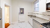 Located at 6300 N Rosebury Ave in Clayton-adjacent St. Louis, this three-bedroom, one-bathroom unit offers a clean, functional layout across a single floor. Warm hardwood floors run throughout the bedrooms and living areas, lending a classic character to the space. The primary bedroom is generously sized and benefits from multiple windows fitted with blinds, allowing ample natural light and views of the surrounding neighborhood. The two additional bedrooms are well-proportioned, each featuring the same hardwood flooring and ceiling fans, making them versatile for various uses. Classic six-panel white interior doors and crisp white trim add a timeless architectural detail throughout. The kitchen stands out with its updated finishes, including white shaker-style cabinetry, granite countertops, subway tile backsplash with a decorative accent border, stainless steel appliances — including a gas range, microwave, and dishwasher — and a porcelain marble-look tile floor. A door in the kitchen provides convenient secondary access. The bathroom features a tub-shower combination with clean white subway tile surround. A hallway connects the rooms, contributing to an efficient and accessible floor plan. The overall aesthetic is bright, neutral, and move-in ready.