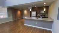 This two-floor space masterfully combines industrial charm with contemporary design. The open-concept main level immediately draws attention with its striking exposed brick accent wall, which adds warmth and texture to the expansive living area. Rich hardwood flooring flows throughout, complementing the space's modern aesthetic.

The kitchen is a standout feature, outfitted with dark espresso cabinetry, granite countertops, and a full suite of stainless steel appliances, including a refrigerator, range, and built-in microwave. A generously sized kitchen island with a granite surface and integrated sink serves as both a functional workspace and a natural gathering point. Stylish pendant lighting hangs above the island, enhancing the area's visual appeal.

Recessed lighting and track lighting are thoughtfully distributed throughout the main level, ensuring the space is well-lit from multiple angles. The open layout between the kitchen and living area creates a seamless flow, making the space feel expansive and connected. The combination of the brick wall, warm wood tones, and modern fixtures gives the interior a distinctive loft-inspired character that balances comfort with urban sophistication across both floors.