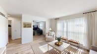 This thoughtfully designed single-floor residence offers a functional and comfortable layout across six distinct rooms. Light-toned hardwood flooring runs throughout, creating a cohesive and airy feel.

The living room is bathed in natural light thanks to a full-width sliding glass door dressed with sheer white curtains and vertical blinds, offering views of the surrounding greenery. A warm, neutral color palette and clean white walls give the space a bright, inviting ambiance.

Adjacent to the living area, a dedicated dining room provides an intimate setting with framed landscape artwork adorning the walls. The kitchen is equipped with warm wood cabinetry, a gas range, full-size refrigerator, and tile backsplash, offering efficient functionality.

The private office is a well-sized, windowed room featuring a ceiling fan and ample workspace, ideal for productive work-from-home arrangements. The bedroom provides a cozy retreat with its own window and natural light access.

The bathroom is finished with classic white subway tile wainscoting, a vanity with medicine cabinet mirror, and a shower-tub combination, maintaining a clean and practical aesthetic throughout.