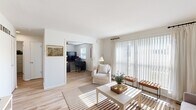 This thoughtfully designed single-floor residence offers a functional and comfortable layout across six distinct rooms. Light-toned hardwood flooring runs throughout, creating a cohesive and airy feel.

The living room is bathed in natural light thanks to a full-width sliding glass door dressed with sheer white curtains and vertical blinds, offering views of the surrounding greenery. A warm, neutral color palette and clean white walls give the space a bright, inviting ambiance.

Adjacent to the living area, a dedicated dining room provides an intimate setting with framed landscape artwork adorning the walls. The kitchen is equipped with warm wood cabinetry, a gas range, full-size refrigerator, and tile backsplash, offering efficient functionality.

The private office is a well-sized, windowed room featuring a ceiling fan and ample workspace, ideal for productive work-from-home arrangements. The bedroom provides a cozy retreat with its own window and natural light access.

The bathroom is finished with classic white subway tile wainscoting, a vanity with medicine cabinet mirror, and a shower-tub combination, maintaining a clean and practical aesthetic throughout.