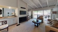 Located at 2400 Harbor Blvd in Costa Mesa, California, this single-story residence offers a thoughtfully designed layout with a cohesive blend of comfort and character. The living room is a standout space, anchored by a striking floor-to-ceiling shiplap fireplace surround, a wall-mounted TV, and distinctive exposed wooden beam ceilings painted white, adding architectural charm throughout. Sliding glass doors open directly to a private outdoor balcony, allowing natural light to pour in and providing seamless indoor-outdoor connectivity with views of surrounding greenery. The kitchen features white cabinetry, granite-style countertops, a gas range, and wood-look vinyl flooring that extends into the hallway and bathroom areas. The dining area offers an intimate setting with rich moodier wall tones and a dark wood dining set beneath original artwork. The bedroom boasts soaring ceilings with exposed beams, plush carpeting, mirrored sliding closet doors, and direct access to an en-suite bathroom with white cabinetry and ample vanity space. A secondary bedroom similarly showcases the beam ceiling design, plentiful natural light, and a tranquil color palette. The full bathrooms are clean and functional, with one featuring a chrome towel bar and classic fixtures. This residence delivers a relaxed California living experience throughout.
