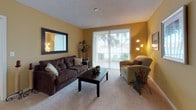 This single-floor residence offers a thoughtfully designed layout with warm, neutral tones and carpet flooring throughout most of the living spaces. The living room features golden-yellow walls, plush carpeting, and a large sliding glass door with vertical blinds that invites natural light and outdoor views. A bold wall mirror and decorative framed artwork add character to the space.

The adjacent dining area accommodates a round wooden table with upholstered chairs beneath recessed lighting, with an entry foyer visible nearby. The kitchen is efficiently arranged with white cabinetry, white appliances including a range and refrigerator, light wood-look flooring, and a built-in desk nook that doubles as a convenient workspace.

Two carpeted bedrooms provide comfortable retreats; the primary bedroom features a dark wood dresser with a large mirror, while the secondary bedroom offers a cozy, well-lit atmosphere. Both bathrooms include tile flooring, vanities with white cabinetry, and bright overhead lighting. A dedicated home office nook with hardwood flooring, a wooden desk, and an upholstered chair offers a quiet workspace. The in-unit laundry area houses a full-size washer and dryer, adding practical convenience.