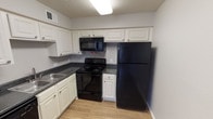 Located in North Richland Hills, Texas, this single-floor unit offers a practical and well-organized layout suited for comfortable everyday living. The living area is a standout space, featuring vaulted ceilings that enhance the sense of openness, wood-look laminate flooring, and a ceiling fan with light fixture. Large windows fitted with horizontal blinds and vertical panel blinds allow natural light to flow in while providing privacy and outdoor views of the surrounding area.

The kitchen is efficiently designed with white cabinetry offering generous upper and lower storage, dark countertops, and a suite of black appliances including a refrigerator, electric range, over-the-range microwave, and a built-in sink. Light wood-look flooring extends through the kitchen, complementing the clean, neutral color palette.

The bedroom features plush carpeting, a ceiling fan with light, a textured ceiling, and a window that brings in natural light. Additional rooms display the same neutral gray tones and wood-look flooring, with tall walls and clearly defined transitions between spaces. The bathroom includes a full tub-shower combination with a showerhead, chrome fixtures, and a brushed nickel grab bar, finished with clean white surroundings throughout.
