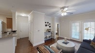 This single-story, 2-bedroom, 2-bathroom residence offers a well-organized layout with consistent design details throughout. The living room serves as the central gathering space, featuring crown molding, dark hardwood-style flooring, a ceiling fan, and French doors that invite natural light while providing outdoor access. Crown molding continues into the adjacent dining area, which is illuminated by a large drum pendant light and connects directly to the kitchen. The kitchen features warm wood cabinetry, granite-style countertops, a double basin sink, and white appliances, including a dishwasher and range. A separate laundry area is accessible from the kitchen. Both bedrooms are carpeted and include ceiling fans and windows with curtains. One bedroom features notably higher ceilings, adding a sense of spaciousness. The two bathrooms include wood-style flooring, white vanity cabinetry with ample storage, large mirrors with overhead lighting, and tub-shower combinations. Neutral, warm beige tones are carried throughout the residence, creating a cohesive and inviting ambiance across all rooms.
