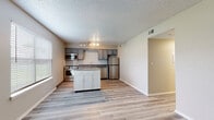 Located at 1108 NE Independence Ave in Lee's Summit, Missouri, this single-story residence offers a well-planned layout with a clean, contemporary aesthetic throughout. The open-concept kitchen serves as a focal point, equipped with stainless steel appliances including a range, microwave, dishwasher, and refrigerator. Gray cabinetry pairs with granite-style countertops and a classic white subway tile backsplash, while a freestanding white island with a butcher block top provides additional prep and storage space. Track lighting and natural light from nearby windows keep the kitchen bright and functional. The kitchen flows naturally into the living area, which features light-toned luxury vinyl plank flooring and a large window that invites natural light and outdoor views. The bedrooms are carpeted for comfort, with one featuring a ceiling fan with light fixture and another offering a double sliding-door closet for ample storage. Two bathrooms mirror each other in design, each finished with gray vanity cabinetry, granite-style countertops, and wood-look flooring. Textured ceilings are consistent throughout, contributing to the space's cohesive, move-in-ready character.