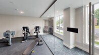 Located at 303 Dunbar St in Manchester, New Hampshire, this well-appointed fitness center offers a comprehensive workout facility within a efficiently organized single-floor layout. The space is divided into distinct functional zones, each designed to support a full range of exercise activities.

The cardio area is equipped with multiple treadmills and elliptical machines, positioned in front of dual wall-mounted flat-screen televisions, allowing users to stay entertained during their workouts. Adjacent to this zone is a strength training area featuring a multi-function cable machine, a stationary bike, and a weight bench, set against bold blue accent walls that lend the space a focused, energetic atmosphere. Structural columns with clean white finishes add architectural character while defining the zones within the open floor plan.

A standout feature of the fitness center is the glass-walled studio or stretching area, enclosed by sleek floor-to-ceiling sliding glass panels. This section benefits from large windows that invite natural light and offer views of the surrounding outdoor landscape, creating a bright and refreshing environment. A wall-mounted television and padded flooring complete this versatile space.

Throughout the facility, dark rubberized flooring provides durability and comfort underfoot. Recessed lighting ensures consistent, well-distributed illumination across the entire space. The overall design is modern and clean, balancing functionality with a polished aesthetic.