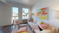 This single-floor unit is designed with a clean, contemporary aesthetic throughout, characterized by white walls, warm wood-tone accents, and durable hardwood-style flooring that flows seamlessly from room to room. The kitchen is thoughtfully outfitted with light wood cabinetry extending to the ceiling for ample storage, a white quartz countertop, a textured penny-tile backsplash, and a full suite of stainless steel appliances including a refrigerator, electric range, built-in microwave, and dishwasher. Adjacent to the kitchen, the dining area provides an intimate setting with space for a small table and opens to the broader living space. The living room is bright and inviting, benefiting from large windows that draw in natural light and offer views of the surrounding neighborhood. The bedroom is a calm retreat, featuring carpet flooring, a window with outdoor views, and ample wall space. The full bathroom includes a soaking tub and shower combination, a wood-finish vanity with a white countertop, a large mirror, and hardwood-style flooring. A dedicated laundry room houses a stacked washer and dryer unit, a multi-drawer dresser, and an overhead wire shelving system for added organization.