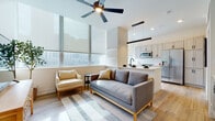 Located at 55 Public Square in the heart of downtown Cleveland, this single-floor residence combines modern design with functional living. The open-concept living and kitchen area serves as the centerpiece of the space, featuring light hardwood flooring, ceiling fans, and expansive windows dressed with roller shades that frame city views and flood the interior with natural light. The kitchen is outfitted with white cabinetry, quartz countertops, a white subway tile backsplash, stainless steel appliances including a built-in microwave, dishwasher, and electric range, and a matte black faucet at the sink. A peninsula with pendant lighting connects the kitchen seamlessly to the living area. A welcoming entryway with a rich wood door and console storage leads into the residence. The hallway, lined with light walls and hardwood flooring, connects the main living areas to the private rooms. The bedroom features plush carpeting, a ceiling fan, and the convenience of an in-unit stacked washer and dryer. The bathroom is finished with large-format tile flooring, a tub-shower combination, and matte black fixtures. Throughout, the design maintains a clean, contemporary aesthetic with a warm, neutral palette.