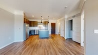 This single-floor residence offers a well-designed open-concept layout that seamlessly connects the kitchen, dining, and living areas. The kitchen serves as the focal point, showcasing rich dark-toned cabinetry with contemporary hardware, stainless steel appliances including a refrigerator, range, and microwave, and a central island topped with light granite countertops. Pendant lighting with sleek black fixtures hangs above the island, adding a modern touch. A tile backsplash and recessed lighting complete the kitchen's polished look.

Warm hardwood-style flooring runs throughout the main living areas, complementing the neutral gray walls and white trim. The spacious living area features a sliding door that opens to a private balcony, offering pleasant outdoor views and an abundance of natural light. A dedicated walk-in closet provides practical storage with built-in rods.

The bedrooms are finished with plush carpet, neutral walls, and white panel doors, creating a calm and comfortable atmosphere. One bedroom features a window with scenic outdoor views, while another includes a double-door closet. Throughout the unit, the clean, modern finishes and thoughtful layout contribute to a cohesive and inviting living environment.