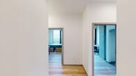 This contemporary high-rise unit is thoughtfully designed with a clean, modern aesthetic that blends functionality with striking architectural character. Throughout the space, light hardwood flooring provides a warm contrast to the exposed concrete ceilings and structural columns, creating an industrial-modern ambiance that feels both refined and livable.

The open living area is a standout feature, anchored by floor-to-ceiling windows that frame expansive panoramic views of the city skyline and waterfront. Natural light floods the room, complementing the minimalist furnishings including a plush sofa, accent chairs, and sleek metal-framed tables.

Multiple bedrooms are accessible via a central hallway, each equipped with a bed, a dedicated study desk and chair, and an open closet area. The bedrooms benefit from large windows offering elevated views of the surrounding cityscape and treetops, making each room feel bright and connected to the outdoors. Exposed concrete columns add a distinctive architectural touch to select rooms.

The kitchen is outfitted with light wood cabinetry, stainless steel appliances including a full-size refrigerator and oven, and ample storage, all set against the continuous hardwood flooring. A clean, efficiently designed bathroom features warm wood vanity cabinetry, a wall mirror, and light tiling, completing this well-appointed urban residence.