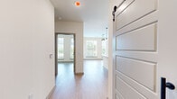 This thoughtfully designed two-bedroom, one-bathroom residence offers a cohesive modern aesthetic across its single floor. Light wood-toned flooring runs throughout, complementing the crisp white walls and creating a clean, contemporary feel.

The kitchen serves as a focal point of the space, showcasing a two-tone design with white upper cabinetry and bold teal lower cabinets, accented by a white subway tile backsplash. A central island with a white countertop and undermount sink provides additional workspace and storage, while stainless steel appliances and globe pendant lighting add polished, functional detail.

The open layout connects the kitchen seamlessly to the living area, which benefits from large windows that invite abundant natural light and offer views of surrounding greenery. A distinctive sliding barn door with black hardware adds an architectural accent to the hallway.

The primary bedroom features a ceiling fan and a wall of tall windows framing outdoor views, creating an airy, light-filled retreat. The second bedroom is compact and well-proportioned, with direct hallway access.

The bathroom is well-appointed with a wood-toned vanity, white quartz countertop, framed mirror, matte black fixtures, and a glass-enclosed walk-in shower with white tile surround. A dedicated closet completes the unit's layout.