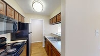 This efficient and thoughtfully designed single-floor unit offers a complete set of rooms within a compact footprint, including a kitchen, bedroom, closet, bathroom, laundry area, and hallway. The kitchen is appointed with warm-toned wood cabinetry, a double stainless steel sink, a gas range, over-the-range microwave, and a stainless steel refrigerator. A pass-through counter with overhead cabinetry opens the kitchen toward the living area, creating an open and connected feel. The living room features light hardwood-style flooring and a fireplace, adding warmth and character to the space. The bedroom is carpeted and includes a ceiling fan with light fixture, a window with blinds allowing natural light, and access to a dedicated closet. The full bathroom is clean and functional, featuring a shower/tub combo with chrome fixtures and hardwood-style flooring. A dedicated laundry area with washer hookups and a storage shelf above provides added convenience. Throughout the unit, textured ceilings, neutral wall tones, and consistent flooring choices contribute to a cohesive and practical living environment.