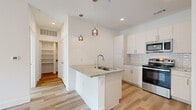 This well-appointed 1-bedroom, 1-bathroom residence showcases a clean, modern design with light wood-style flooring that flows seamlessly throughout every room. The open-concept kitchen serves as a central highlight, featuring a peninsula island with a granite countertop and an undermount sink, pendant lighting overhead, crisp white cabinetry, a subway tile backsplash, and a full suite of stainless steel appliances. The layout connects the kitchen naturally to the living area, which benefits from a ceiling fan and access to natural light through a glazed door and adjacent window. The bedroom is a comfortable, sun-filled space with a ceiling fan, a window with blinds, and direct access to a generously sized walk-in closet outfitted with dual hanging rods and built-in shelving. The bathroom is well-finished, offering a granite-topped vanity with white cabinetry, a marble-surround soaking tub and shower combination, and hardwood-style flooring that continues the cohesive aesthetic. A hallway connects the main rooms efficiently. Throughout the unit, white walls, recessed lighting, and consistent finishes create a bright, cohesive, and move-in-ready atmosphere.