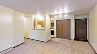 This single-floor unit offers a functional and open layout that connects the living area to the kitchen through a half-wall pass-through, creating a sense of openness while maintaining defined spaces. The living area is finished with wall-to-wall carpet in a neutral tone, providing a comfortable and cohesive foundation throughout the space.

The kitchen is equipped with warm wood-toned cabinetry, a white refrigerator, and stainless steel appliances including a range and built-in microwave. The pass-through counter enhances interaction between the kitchen and living areas, making the space practical for everyday use.

Track lighting mounted on the ceiling provides targeted illumination, complementing the flush ceiling light fixture in the kitchen area. The textured ceiling adds dimension to the interior, while neutral-toned walls keep the space feeling bright and versatile.

A large sliding closet with a dark wood-paneled door offers generous storage directly within the main living area, adding a convenient organizational feature. The overall layout is straightforward and well-appointed, suitable for comfortable day-to-day living.