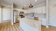 Located at 888 Delaware Ave in Buffalo, NY, this single-floor unit offers a thoughtfully designed layout with contemporary finishes throughout. The open-concept kitchen serves as the centerpiece of the space, showcasing crisp white shaker cabinetry, striking marble-look countertops, and a large central island perfect for dining or food preparation. Stainless steel appliances — including a refrigerator, range, microwave, and dishwasher — complement the kitchen's modern aesthetic, while industrial-style pendant lighting adds a warm, inviting contrast. Light hardwood flooring flows seamlessly throughout the unit, lending a clean and cohesive look to every room. The living areas are bright and airy, benefiting from large windows that allow generous natural light to pour in, with views of the surrounding Buffalo neighborhood adding character and context to the space. The bedroom is generously proportioned, featuring the same hardwood flooring and neutral wall tones that create a calm, versatile environment. The bathroom is well-appointed with a glass-enclosed walk-in shower featuring white subway tile, a rain showerhead, and chrome fixtures, paired with a white vanity topped with a dark stone countertop and a large mirror. The overall aesthetic is clean, modern, and move-in ready.