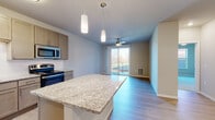 Located at 146 Westgate Mall in Madison, Wisconsin, this single-floor unit offers a thoughtfully designed open-concept layout that seamlessly connects the kitchen, dining, and living areas. The kitchen is a standout feature, showcasing a large granite-topped center island with pendant lighting overhead, custom taupe cabinetry extending to the ceiling, a full suite of stainless steel appliances including a refrigerator, range, microwave, and dishwasher, and a classic white tile backsplash. Light hardwood flooring flows throughout the main living areas, contributing to a clean, contemporary aesthetic. The living area is bright and airy, anchored by a ceiling fan and a sliding glass door that opens to a private balcony with outdoor views. The bedroom is carpeted for comfort, features a ceiling fan, a closet, and a window that brings in natural light. The bathroom is finished with wood-tone cabinetry, granite countertops, an undermount sink with brushed nickel fixtures, and light hardwood-style flooring. Neutral wall tones throughout the unit create a calm, cohesive atmosphere well-suited for modern living in the heart of Madison.