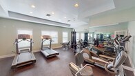Located along Chapel Lakes Drive in Wetumpka, Alabama, this fitness center offers a thoughtfully organized workout environment designed to support a full range of exercise routines. The single-floor facility features soft sage-green walls, white trim, and a tray ceiling with recessed lighting that creates a clean, well-lit atmosphere throughout. Dark rubber flooring provides both durability and safety underfoot across the entire space.

The cardio area is well-stocked with multiple treadmills, elliptical trainers, and a stationary bike, positioned to take advantage of natural light from several windows fitted with white blinds. A multi-station cable machine anchors the strength-training zone, accompanied by a full dumbbell rack ranging across multiple weights, step platforms, and a workout bench. Large wall-mounted mirrors span a significant portion of the room, visually expanding the space and allowing users to monitor their form during exercise.

The facility is accessed through French doors and connects to an adjacent common area. Adequate ventilation is provided through ceiling-mounted HVAC vents. Overall, the space maintains a practical and accessible layout suited for both cardio-focused and strength-training workouts.