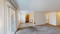 Located at 12514 SE 7th St in Vancouver, Washington, this one-bedroom, one-bathroom unit offers a practical and well-organized single-floor layout. The galley-style kitchen is efficiently designed with oak-trimmed white cabinetry lining both walls, providing ample storage space. White appliances — including an electric range with overhead microwave and a dishwasher — complement the light countertops and tile flooring, creating a clean, functional workspace. A hallway leads from the kitchen toward the remaining rooms, maintaining a logical flow throughout the unit. The generously sized primary bedroom features plush wall-to-wall carpeting, a wide sliding mirrored closet, and a window overlooking greenery outside, allowing natural light to fill the room. An additional carpeted room with a standard closet offers flexible use as a secondary living or storage space. The bathroom is bright and clean, featuring a wide vanity with oak cabinetry, a large mirror, skylight-style overhead lighting, and tile flooring. A dedicated utility room adds everyday convenience. Throughout the unit, neutral white walls and consistent finishes create a cohesive and move-in ready environment suited for comfortable living.