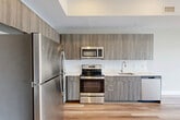 Located at 960 Greene St in Ann Arbor, MI, this modern 1-bedroom, 1-bathroom unit offers a well-designed layout across a single floor. The open-concept kitchen and living area serves as the heart of the space, featuring light hardwood flooring that carries throughout most of the unit. The contemporary kitchen is equipped with stainless steel appliances, including a full-size refrigerator, electric range, built-in microwave, and dishwasher. Flat-front cabinetry in a warm wood-tone finish extends to the ceiling, maximizing storage, while light countertops and a clean tile backsplash contribute to the space's crisp, modern aesthetic. Floor-to-ceiling windows in the living area invite an abundance of natural light and offer views of the surrounding neighborhood. The bedroom is carpeted for comfort and features a large window with urban views, maintaining the unit's bright and airy atmosphere. The bathroom mirrors the modern design language with wood-tone vanity cabinetry, a white countertop, and hardwood-style flooring. Additional practical features include two closets and an in-unit laundry area, rounding out this efficiently planned and thoughtfully finished residential space.