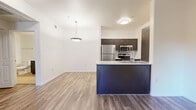 Located at 2656 W Broadway Blvd in Tucson, Arizona, this one-bedroom, one-bathroom apartment offers a well-designed single-floor layout with a clean, modern aesthetic throughout. The open-concept living and kitchen area forms the heart of the unit, where wood-style plank flooring, crisp white walls, and a pendant light fixture create a bright and welcoming atmosphere. The kitchen is outfitted with dark espresso cabinetry, a full suite of stainless steel appliances including a refrigerator, microwave, and range, and a peninsula with a built-in sink and light countertop that doubles as a breakfast bar. The living area flows naturally from the kitchen, offering an open and flexible layout. The bedroom is a comfortable, well-proportioned space featuring a ceiling fan, wood-style flooring, and access to a walk-in closet with built-in shelving. A smart thermostat is conveniently located in the living area, and an in-unit washer and dryer add practical convenience. The bathroom features a full tub-shower combination, a dark vanity with a light stone-topped countertop, and tile flooring. Throughout the unit, tall ceilings and neutral tones contribute to a sense of openness and ease.