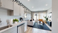 This single-floor residence showcases a thoughtfully designed open-concept layout where the kitchen flows seamlessly into the living area. The kitchen is outfitted with stainless steel appliances—including a full-size refrigerator, electric range, built-in microwave, and dishwasher—complemented by granite-look countertops, white shaker-style cabinetry, and light wood-tone flooring that extends throughout the unit.

The living area is anchored by a striking bold black-and-white graphic accent wall, creating a dynamic focal point. Large windows dressed with sheer curtains and wood blinds allow generous natural light to fill the space. A glass-top coffee table, neutral sofa, and leather accent chair complete the contemporary furnishings.

The bedroom features its own distinctive patterned accent wall in a vertical geometric design, a closet, wall-mounted television, and warm ambient lighting. A full bathroom with a tub-shower combination and matching wood-tone flooring rounds out the unit.

A wide, well-lit entry corridor with recessed lighting and built-in storage doors provides a clean, organized transition into the main living spaces, reinforcing the unit's modern and functional design throughout.