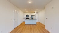 Located at 1010 Rosefinch Landing in Hoschton, Georgia, this single-floor residence offers a clean, contemporary design with an open and functional layout. The heart of the home is a well-appointed kitchen featuring white shaker-style cabinetry with brushed hardware, granite countertops, a central island with an undermount sink, and a full suite of stainless steel appliances including a French door refrigerator, electric range, built-in microwave, and dishwasher. Recessed lighting illuminates the space, which flows seamlessly into the open living area. Light-toned hardwood-style flooring extends throughout the main living areas, lending warmth and cohesion to the space. The living area is bright and open, benefiting from large windows fitted with horizontal blinds that allow ample natural light while maintaining privacy. A door provides direct access to an exterior area. The bedrooms offer plush carpeting, ceiling fans with integrated lighting, and generous windows that further enhance the sense of light and openness. The interior palette throughout is a crisp, neutral white, creating a clean and versatile canvas. Overall, the home presents a modern, move-in-ready aesthetic with quality finishes and a practical, open floor plan well-suited to everyday living.