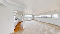 This 1-bedroom, 2-bathroom residence offers a thoughtfully organized single-floor layout filled with natural light and sweeping urban skyline views. The open-concept living room is a standout feature, anchored by a broad band of floor-to-ceiling windows that frame panoramic city and waterfront vistas. Neutral carpet flooring and clean white walls create a bright, airy ambiance throughout the living and sleeping areas.

The kitchen is positioned adjacent to the living room, connected via a convenient pass-through counter that adds an open feel. It features stainless steel countertops, white cabinetry, a full-size refrigerator, and a deep stainless sink — a practical and efficient workspace.

The primary bedroom is generously proportioned, with plush carpet flooring, a large picture window offering city views, and a double-door closet providing ample storage. The room's clean lines and neutral palette make it a calm and functional retreat.

Both bathrooms are well-appointed; one features full grey subway tile surround, a soaking tub with overhead shower, a wall-mounted sink, and a window that brings in natural light. The hallway connects all spaces efficiently, contributing to the unit's logical and livable flow. Overall, the space presents a clean, functional, and light-filled urban living environment.