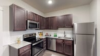 Unit 4107 is a single-floor residence offering a thoughtfully designed open-concept layout that seamlessly connects the kitchen, dining, and living areas. The kitchen is a functional centerpiece, outfitted with rich dark espresso cabinetry, granite-style countertops, a subway tile backsplash, and a full suite of stainless steel appliances including a refrigerator, electric range, built-in microwave, and dishwasher. Generous upper and lower cabinet storage provides ample organization space.

Wood-style plank flooring extends throughout the main living areas, lending warmth and visual continuity to the space. The open living and dining area benefits from large windows that invite natural light, creating a bright and welcoming atmosphere. A ceiling fan with light fixture adds both comfort and practicality to the living space.

The bedroom is a calm retreat, featuring the same wood-style flooring, a ceiling fan, and a well-sized window for natural light. The bathroom is finished with matching dark cabinetry, granite-style countertops, and a tub-shower combination, maintaining the cohesive aesthetic found throughout the unit. Overall, the space presents a modern, neutral palette with consistent finishes that contribute to a clean and comfortable living environment.