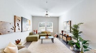 This single-floor residence offers a thoughtfully designed layout that balances comfort and functionality throughout. The living room serves as the centerpiece of the home, featuring wood-style flooring, a ceiling fan with light fixture, neutral-toned walls, and a large window fitted with slatted blinds that allow natural light to fill the space. Bold abstract artwork and lush indoor plants add character and warmth to the room's contemporary aesthetic.

The kitchen is a standout feature, showcasing granite countertops, a large island with pendant lighting overhead, white upper cabinetry paired with gray lower cabinets, a subway tile backsplash, and a full suite of stainless steel appliances including a refrigerator, range, microwave, and dishwasher. Wood-style flooring continues throughout this space, reinforcing the cohesive design.

The bedroom is a tranquil retreat, finished with plush carpet, a ceiling fan, natural light from a window, and ample space for furnishings. A second bedroom provides equal comfort with carpet flooring, a window with outdoor views, and a ceiling fan.

The bathroom is clean and functional, offering a tiled tub-and-shower combination and wood-look flooring. A dedicated in-unit laundry room houses a full-size washer and dryer alongside overhead wire shelving for added storage convenience.