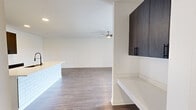 This single-story unit at The E in Whitestown, Indiana, offers a thoughtfully designed open-concept layout that efficiently maximizes its interior footprint. The combined kitchen and living area serves as the heart of the space, featuring durable wood-style flooring, crisp white walls, and a ceiling fan that enhances airflow throughout. French doors in the living area invite natural light and provide access to a private outdoor balcony.

The kitchen is a standout feature, showcasing dark espresso cabinetry with matte black hardware, bright white countertops, and a subway tile-accented island with an integrated sink. Stainless steel appliances, including a refrigerator, range, and microwave, complete the functional and modern aesthetic. A sliding barn door adds a stylish architectural detail connecting key spaces.

The generously sized primary bedroom is finished with plush carpet and a window that allows natural light to fill the room. Two full bathrooms reflect consistent design choices, with wood-toned vanity cabinetry, white countertops, and wood-style flooring. A dedicated laundry room accommodates a full-size washer and dryer with additional overhead cabinetry for storage, adding to the unit's overall practicality.