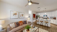 Located at 16333 Columns Way in Baton Rouge, Louisiana, this single-floor residence offers a thoughtfully designed 2-bedroom, 2-bathroom layout with a clean, modern aesthetic. A welcoming entryway with wood-style flooring leads into an open-concept living and kitchen area filled with natural light. The living room features a ceiling fan, large windows with sheer curtains, and ample space for comfortable furnishings. The kitchen is a standout, boasting white shaker cabinetry, granite countertops, a subway tile backsplash, stainless steel appliances, and a center island with bar seating illuminated by pendant lighting. The primary bedroom is generously sized, featuring plush carpeting, large windows, and access to a well-appointed bathroom with granite vanity countertops, a tiled tub-shower combination, and wood-style flooring. A spacious walk-in closet with wire shelving provides excellent storage. The second bedroom is equally bright and comfortable. Additional highlights include a dedicated laundry area with a stacked washer and dryer, a second full bathroom, and consistent wood-style flooring throughout the main areas. The overall ambiance is light, neutral, and contemporary.