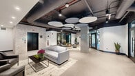 Located at 144 N Main St in Dublin, PA, this thoughtfully designed amenity floor offers a dynamic blend of wellness, recreation, and social spaces across a single expansive level. The welcoming lobby entrance features circular acoustic ceiling panels, polished concrete floors, and an open lounge area furnished with contemporary seating and patterned area rugs, setting an immediately sophisticated tone. The space flows naturally into a communal lounge and social hub, where wave-form acoustic ceiling baffles in deep blue tones create a striking visual canopy above comfortable seating arrangements, a billiards table, and large windows that invite abundant natural light and outdoor views. An adjacent kitchen and dining area includes stainless steel appliances, tile backsplash, and a dining table for group gatherings. The state-of-the-art fitness center is a standout feature, divided into distinct zones for cardio and strength training. Honeycomb-shaped LED lighting fixtures illuminate rows of treadmills and ellipticals, a functional training rig with cable systems, free weights, and a Smith machine. Floor-to-ceiling mirrors, rubber flooring, and mounted televisions enhance the workout experience. A dedicated reception area with a slatted wood desk and bold nature-inspired wall murals adds a unique, artistic touch throughout. This facility is a comprehensive, design-forward destination built for active community living.