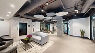 Located at 144 N Main St in Dublin, PA, this thoughtfully designed amenity floor offers a dynamic blend of wellness, recreation, and social spaces across a single expansive level. The welcoming lobby entrance features circular acoustic ceiling panels, polished concrete floors, and an open lounge area furnished with contemporary seating and patterned area rugs, setting an immediately sophisticated tone. The space flows naturally into a communal lounge and social hub, where wave-form acoustic ceiling baffles in deep blue tones create a striking visual canopy above comfortable seating arrangements, a billiards table, and large windows that invite abundant natural light and outdoor views. An adjacent kitchen and dining area includes stainless steel appliances, tile backsplash, and a dining table for group gatherings. The state-of-the-art fitness center is a standout feature, divided into distinct zones for cardio and strength training. Honeycomb-shaped LED lighting fixtures illuminate rows of treadmills and ellipticals, a functional training rig with cable systems, free weights, and a Smith machine. Floor-to-ceiling mirrors, rubber flooring, and mounted televisions enhance the workout experience. A dedicated reception area with a slatted wood desk and bold nature-inspired wall murals adds a unique, artistic touch throughout. This facility is a comprehensive, design-forward destination built for active community living.