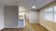 This single-floor unit offers a clean, modern aesthetic with a neutral color palette and durable wood-look flooring throughout the main living areas. The kitchen is a standout feature, outfitted with crisp white shaker-style cabinetry, grey countertops, and a full suite of stainless steel appliances including an electric range, dishwasher, and refrigerator. A peninsula countertop provides additional prep space and a natural division between the kitchen and the adjoining living area. The living space is bright and open, benefiting from large windows that invite natural light and offer views of the surrounding greenery. Baseboard heating is present throughout, ensuring year-round comfort. A dedicated in-unit laundry area with stacked washer and dryer adds everyday convenience. The full bathroom is well-appointed with white cabinetry, grey countertops, and a tub-shower combination. Additional rooms feature plush carpeting, recessed lighting, and generous closet space, offering flexible options for bedrooms or a home office. The textured ceilings and clean white trim tie the space together, creating a cohesive and functional living environment throughout.