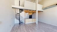 Located at 500 E Third St in downtown Dayton, Ohio, this two-bedroom, three-bathroom loft-style unit spans two floors and showcases a striking blend of industrial character and modern updates. The main floor opens into a spacious living area defined by soaring ceilings, large arched windows with exposed brick surrounds that flood the space with natural light, and durable wood-look flooring throughout. A dramatic spiral staircase serves as a focal point, connecting the main level to the upper floor. The open-concept kitchen features warm wood cabinetry, stainless steel appliances including an electric range, a central island with a sink, and convenient open shelving for additional storage. Exposed metal ductwork and structural beams reinforce the building's industrial heritage. Hallways lined with the same flooring and visible ductwork lead to well-proportioned bedrooms with high ceilings and ample wall space. The three bathrooms are finished with wood-toned vanities, ornate-framed mirrors, and tub-shower combinations. A dedicated laundry room houses a full-size washer and dryer. The upper level provides additional living or sleeping space with its own sense of separation and privacy, making this a versatile and characterful urban residence.