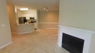 This single-floor residence offers a bright and functional open-concept layout that seamlessly connects the living and kitchen areas. The living room is anchored by a classic white-mantled fireplace, adding warmth and a traditional focal point to the space. Soft carpeting extends throughout the main living area, creating a comfortable and inviting atmosphere, while tile flooring transitions into the kitchen zone.

The kitchen is thoughtfully designed with a curved peninsula countertop finished in granite, providing both prep space and a casual dining area. Stainless steel appliances, including a refrigerator, microwave, and range, give the kitchen a modern and polished look. Cabinetry in a warm neutral tone complements the overall color palette of the home.

Crown molding runs along the ceiling throughout, lending an architectural refinement to the interior. Track lighting in the kitchen and living area provides practical illumination, while the warm beige and cream tones used on the walls and floors create a cohesive, understated elegance. The open sightlines between the kitchen and living space make the layout feel expansive and well-suited for both everyday living and entertaining.