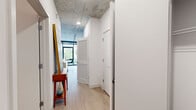 Located at 4557 N Sheridan Rd in Chicago's Uptown neighborhood, this single-floor unit showcases a thoughtfully designed modern interior with industrial-inspired architectural details. The exposed concrete ceiling is a defining feature throughout the space, lending an urban loft aesthetic that contrasts elegantly with the crisp white walls and light hardwood-style flooring.

The living area is anchored by expansive floor-to-ceiling windows that flood the space with natural light and offer direct views of the surrounding streetscape and Chicago architecture. A split-system climate unit is discreetly mounted on the wall, and a structural concrete column adds to the raw, contemporary character of the room.

The kitchen is well-appointed with two-tone cabinetry — high-gloss white upper cabinets paired with gray lower cabinets — complemented by a subway tile backsplash, stainless steel appliances including a French door refrigerator, gas range, dishwasher, and microwave, and a clean white countertop with an undermount sink.

The hallway connects to additional rooms and features louvered doors, offering practical storage solutions. The bathroom is finished with large-format gray floor tiles, full-height white subway tile surrounding the soaking tub and shower, and clean, minimalist fixtures, completing the cohesive modern aesthetic of the space.
