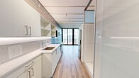 Unit 1403 at 3zero3 in Seattle, Washington is a thoughtfully designed studio residence that maximizes every inch of its compact footprint. The open layout flows from the galley-style kitchen through the main living area to a wall of floor-to-ceiling sliding glass doors that open onto a private balcony, flooding the interior with natural light and framing sweeping views of the Seattle skyline, including a glimpse of the iconic Space Needle.

The kitchen is outfitted with white cabinetry, open shelving, a white quartz countertop, an undermount sink, and stainless steel appliances including a full-size refrigerator, electric range, and over-the-range microwave. Warm wood-tone flooring runs throughout the main living area, complementing the crisp, minimalist aesthetic.

The main living space features a large textured wall panel system that conceals integrated storage and flexible fixtures, paired with a smart home thermostat and direct balcony access. The bathroom is finished in large-format marble-look tile, with a wall-mounted basin, a backlit vanity mirror, and a frameless glass walk-in shower, creating a clean and sophisticated feel. This unit offers a modern urban living experience in the heart of Seattle's Belltown neighborhood.