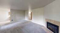 Located at 7412-7416 Golden Given Rd E, Unit 13 in Tacoma, WA, this two-bedroom, two-bathroom residence offers a practical and comfortable single-floor layout. The spacious living room serves as the focal point of the home, featuring plush gray carpeting, neutral-toned walls, and a tile-surround fireplace that adds warmth and character. A window with vertical blinds allows natural light to fill the room, and a dedicated laundry area is conveniently accessible from the living space. The galley-style kitchen is well-equipped with warm wood cabinetry lining both walls, light countertops, tile flooring, and white appliances including an electric range, refrigerator, and dishwasher. Ample cabinet storage makes the kitchen both functional and organized. Both bedrooms are carpeted and feature neutral walls, with the primary bedroom offering a sliding-door closet and a window overlooking the outdoors. Each bedroom is served by its own bathroom, both finished with wood-toned vanity cabinetry, light countertops, and tile flooring. Throughout the unit, warm wood-toned doors and trim create a cohesive, inviting aesthetic. This well-laid-out residence offers a comfortable living experience in a convenient Tacoma location.